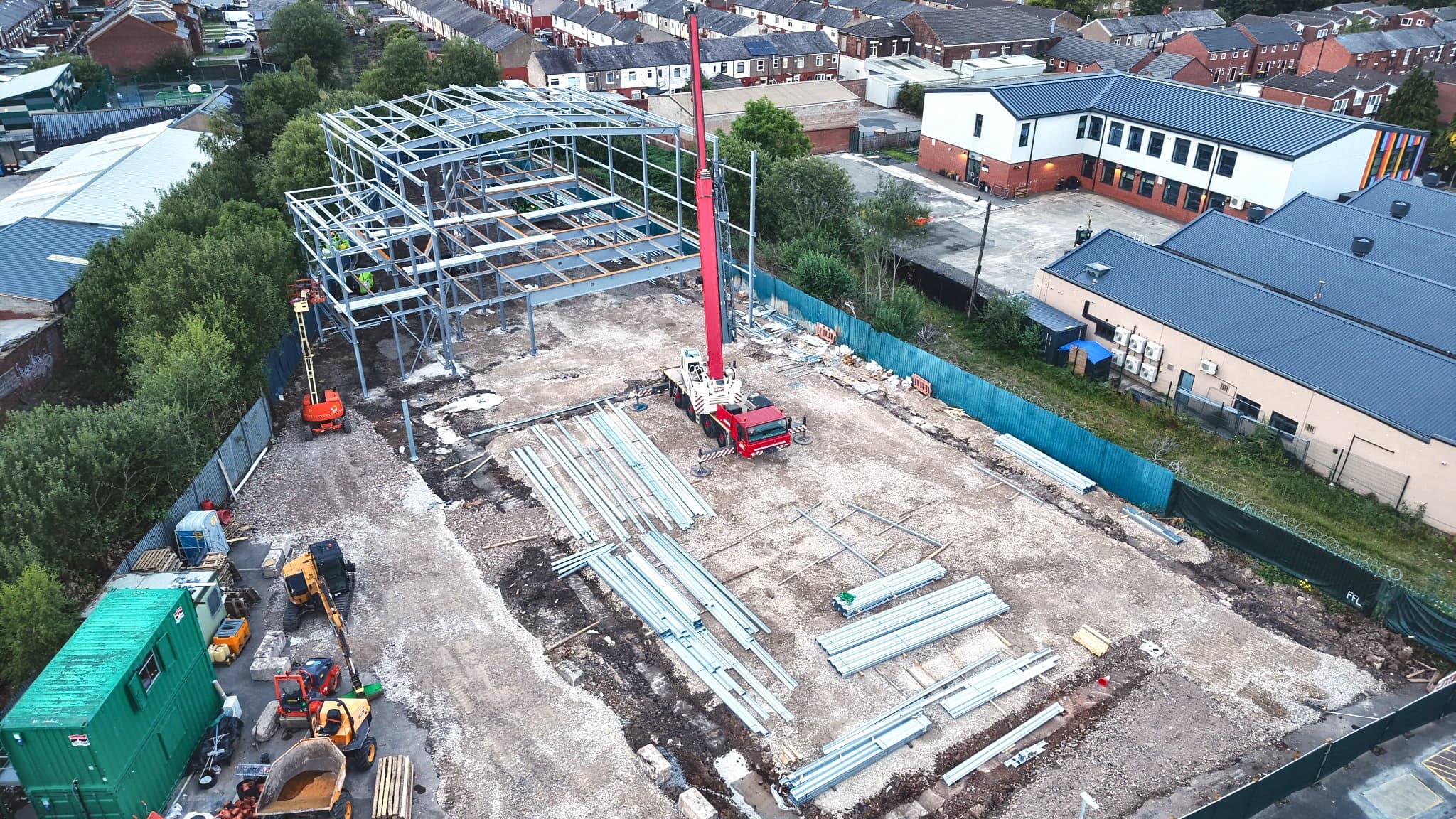 The Quwwat Academy site under construction: a steel frame part-erected over a cleared plot, with a mobile crane, site cabins and stacked steelwork.